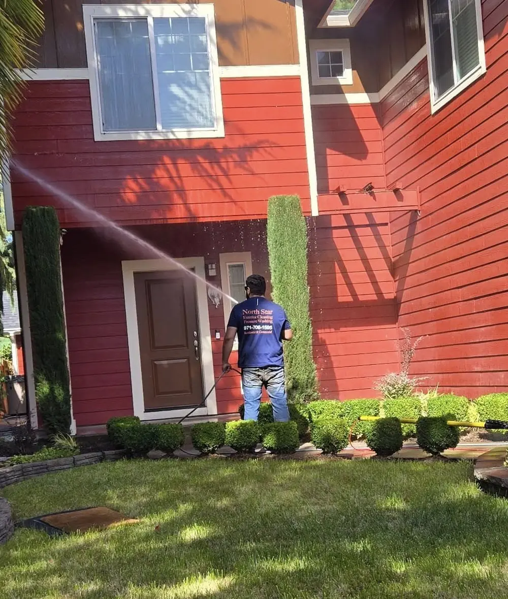 North Star Exterior Cleaning technician pressure washing the siding of a two-story home