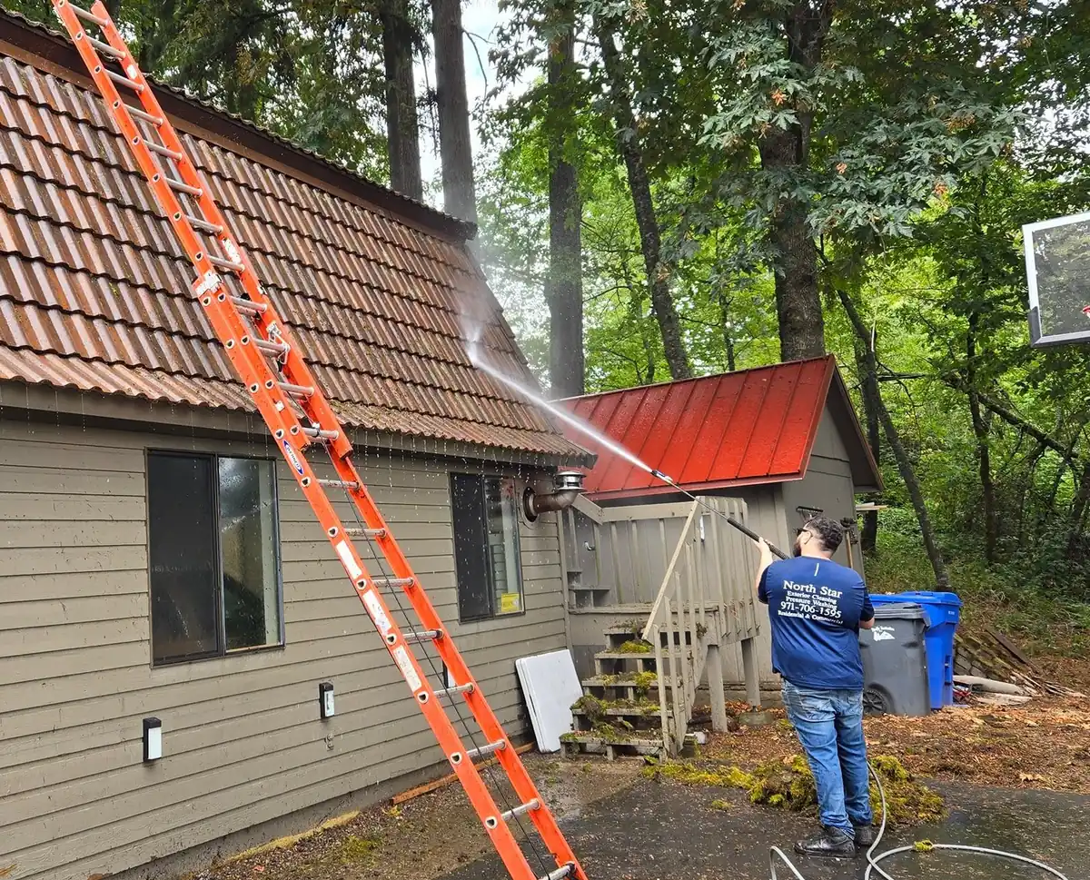 North Star Exterior Cleaning technician on a ladder pressure washing a tile roof