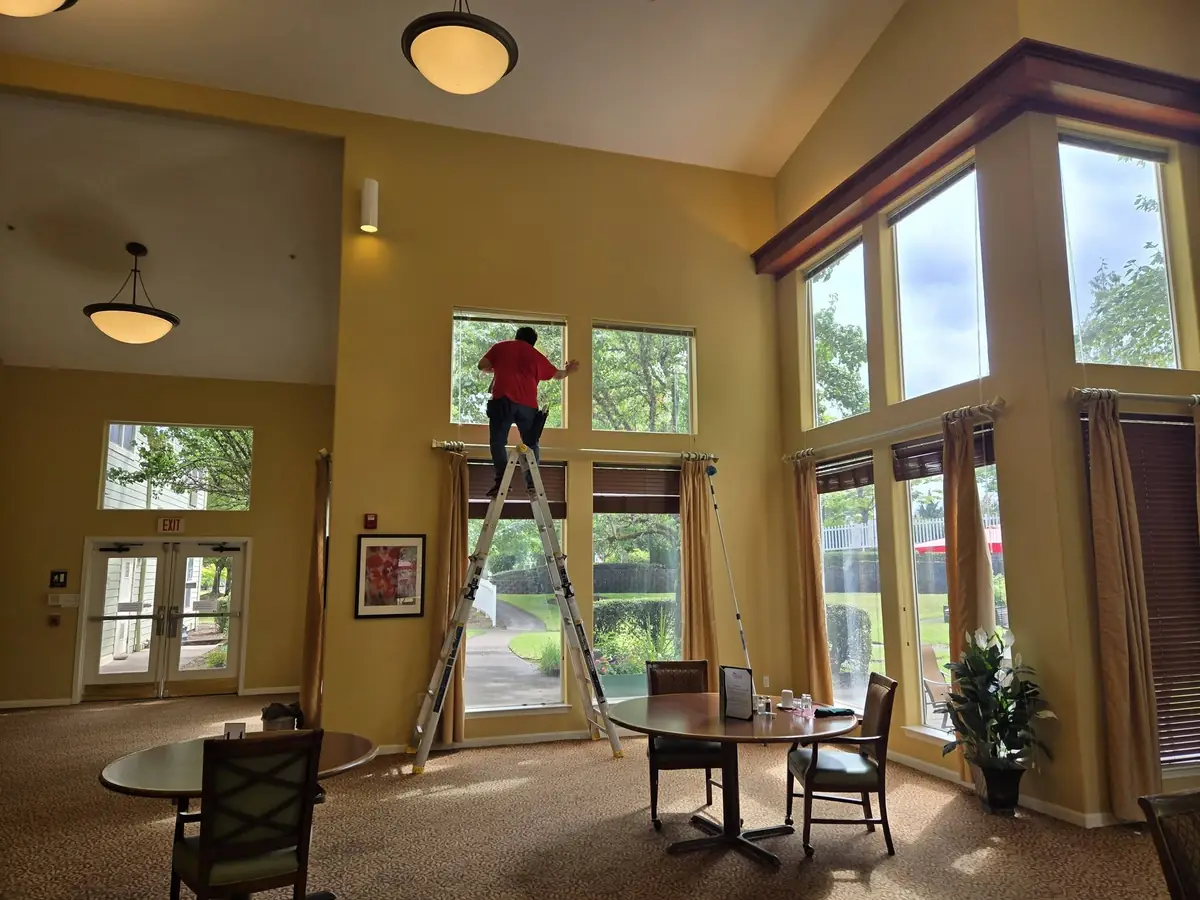 Technician on a ladder cleaning interior windows in a community dining room