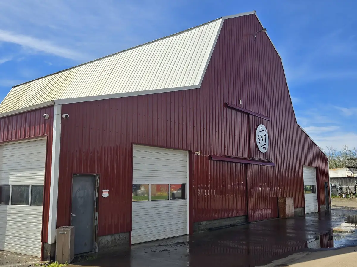 Large red metal barn with white doors after a full exterior wash